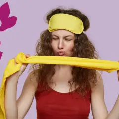Une femme aux cheveux bouclés, portant un masque de nuit jaune, tient un tissu jaune. Elle semble prête pour une coiffure protectrice nuit.