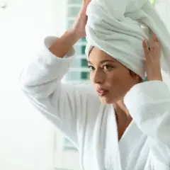 Femme en peignoir blanc, serviette sur la tête, réfléchissant sur le bain d'huile cheveux combien de temps.