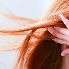 Chevelure rousse flamboyante, une main effleure les mèches. Quelle coloration pour enlever le roux ?