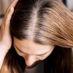 Une femme examine ses racines grasses, cherchant une solution pour sa cure de sebum. Ses mains touchent ses cheveux bruns.