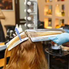 Coiffure : une main gantée applique une décoloration sur des mèches fines, une technique pour comment faire ses racines quand on a des mèches.