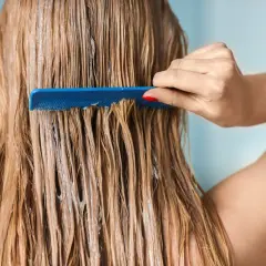 Une main peigne des cheveux colorés, humides et couverts d'un masque à l'argile verte.