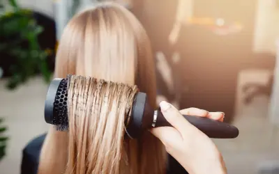 Main d'un coiffeur effectuant un brushing sur des cheveux blonds.