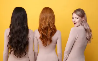 Trois femmes se tiennent côte à côte, montrant la diversité de la couleur cheveux femme : brun foncé, roux flamboyant et blond rosé.