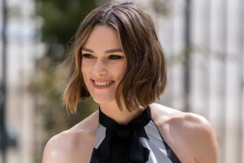 Une femme souriante, la cinquantaine, arbore une coupe dégradée qui donne du volume à ses cheveux fins et plats.