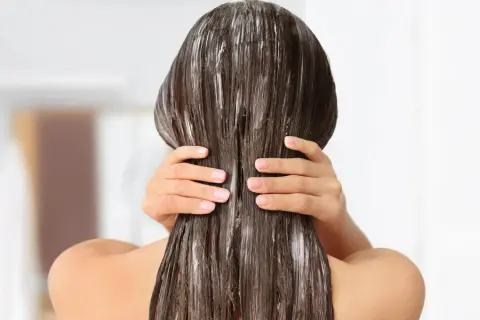 Application d'un masque pour sceller l'hydratation des cheveux. Les mains massent le produit sur les longueurs brunes et humides.