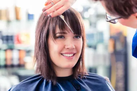Une coiffeuse ajuste la frange d'une cliente souriante, finalisant une coupe carré.