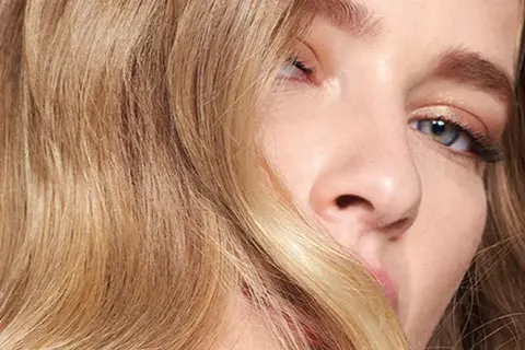 Un gros plan sur le visage d'une jeune femme aux yeux bleus et aux cheveux blond vénitien ondulés, encadrant son visage.