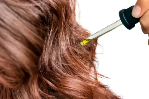 Une goutte d'huile tombe sur des cheveux bruns. Un geste simple pour mettre de l'huile sur les cheveux tous les jours pour les nourrir.