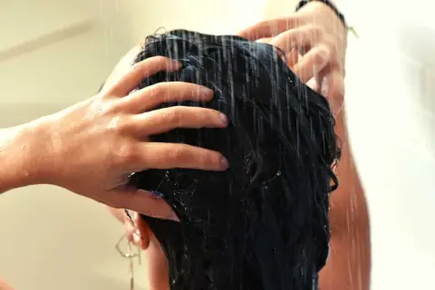 Mains massant des cheveux mouillés sous la douche, comme un soin au beurre de karité cheveux sans rinçage pour une douceur intense.