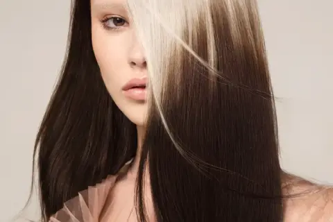 Une femme au regard intense, ses longs cheveux bruns contrastent avec des mèches blondes lumineuses. Un balayage inversé avant après spectaculaire.