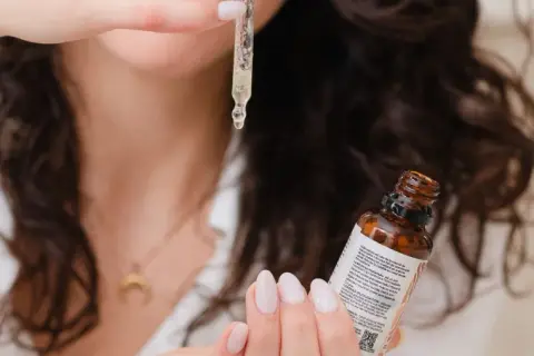 Une femme montre comment appliquer un sérum avec une pipette, une goutte dorée tombant sur sa main.