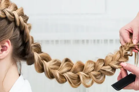 Une main peigne une tresse blonde, une coiffure originale facile à réaliser pour un look sophistiqué.