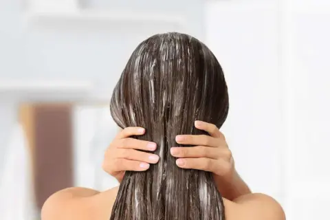 Application d'un soin pour une clarification cheveux. Les mains appliquent le produit sur les longueurs.