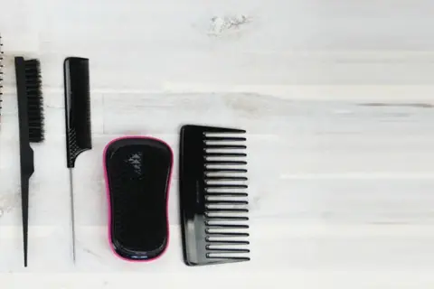 Ensemble de brosses et peignes pour cheveux, dont une brosse à cheveux gras, sur fond de bois clair.