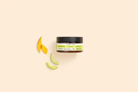 Un pot de beurre de soin cheveux Aroma-Zone, avec des tranches de mangue et d'avocat à côté.