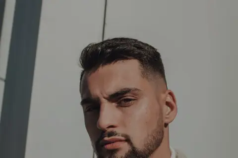 Un homme au chignon homme rasé, regard intense, sous un soleil éclatant.
