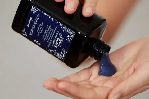 Une main verse un shampoing bleu, idéal pour les cheveux blonds, dans une autre main.