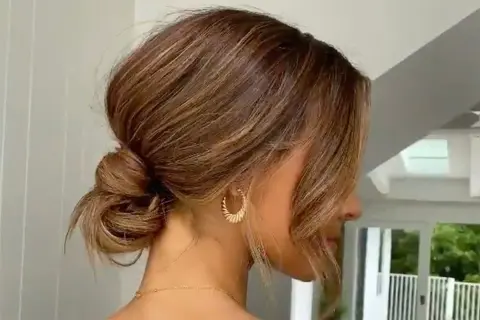 Une coiffure élégante avec un chignon bouclé flou, des mèches encadrant le visage et des boucles d'oreilles dorées.