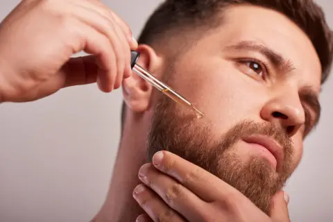 Un homme applique de l'huile de ricin sur sa barbe avec un compte-gouttes pour une pousse plus dense et soyeuse.
