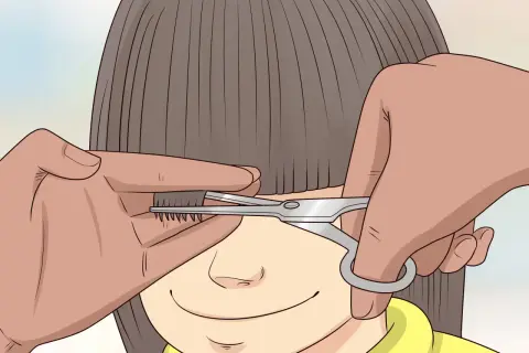 Une main tient une mèche de cheveux d'un enfant pour un couper cheveux enfant. Des ciseaux s'approchent pour la coupe.