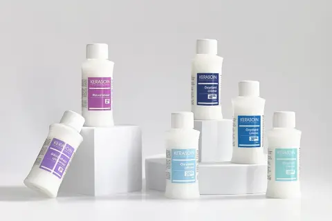 Six bouteilles de produits capillaires Kerasoin, dont un révélateur couleur, disposées sur des cubes blancs.
