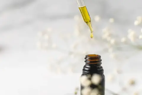 Goutte d'huile de jojoba tombant d'une pipette sur un flacon ambré. Idéal pour des cheveux transformés, avant après.