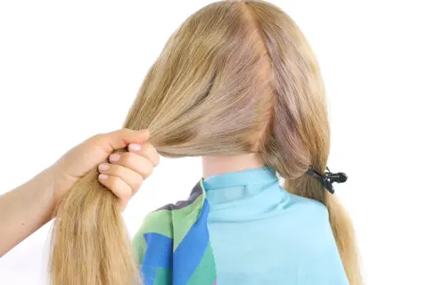 Main d'une femme tenant une mèche de cheveux blonds pour commencer une tresse hollandaise.
