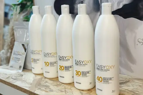 Cinq bouteilles d'oxydant crème universel, dont une de 40 volumes, sont alignées. Ce peroxyde d'hydrogène est enrichi en huile de reine des prés.