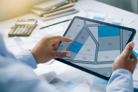 Une personne examine un plan de parcelle sur une tablette, calculant peut-être combien coûte une permanente pour un projet.