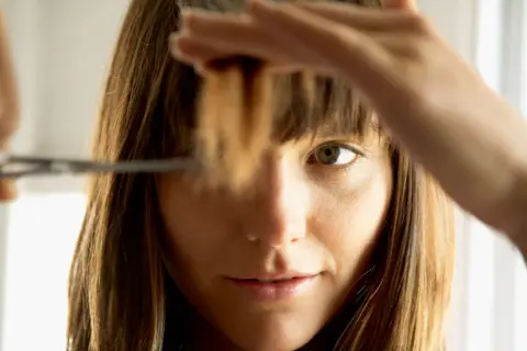 Une femme se coupe les pointes des cheveux. Elle hésite sur combien de cm couper.