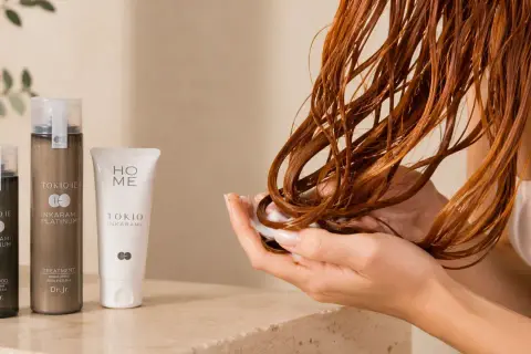 Mains douces appliquant un soin sur des cheveux bouclés roux, avec des produits Tokio Inkarami. Idéal pour la décoloration cheveux bouclés.