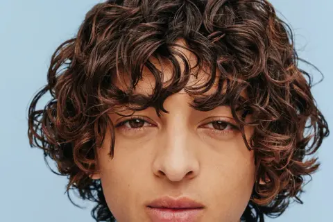 Gros plan sur un visage aux yeux marron et à la coiffure cheveux frisés bruns et volumineux.