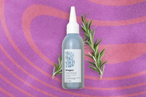 Flacon d'huile de romarin pour la pousse des cheveux, entouré de brins de romarin frais sur fond pailleté rose et violet.