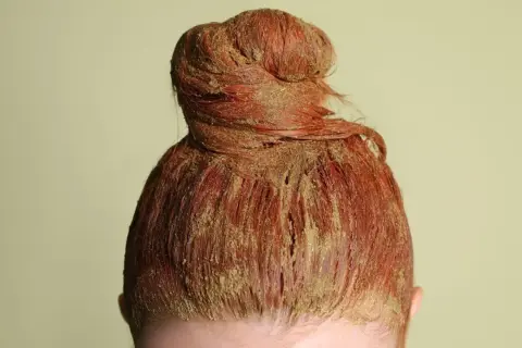 Chevelure rousse en chignon, recouverte d'une pâte de coloration végétale blonde.