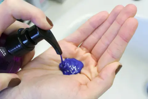 Une main pompe un shampoing bleu vif dans une paume ouverte. Le produit est prêt à être utilisé pour un avant-après spectaculaire.