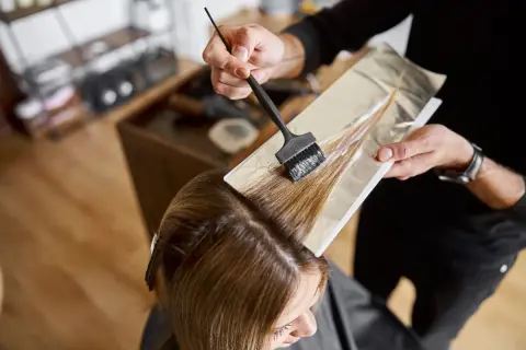 Coiffeur appliquant de la poudre décolorante et oxydant 30 dosage sur des mèches de cheveux, préparant une transformation capillaire.
