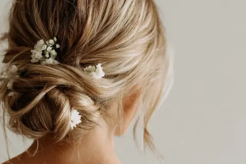 Chignon flou et romantique sur cheveux mi-longs, orné de petites fleurs blanches.