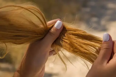Mains tenant des cheveux blonds, légèrement humides, comme après un passage à la mer.
