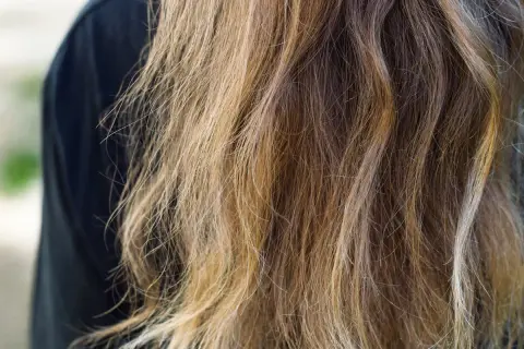Cheveux longs et ondulés, d'une teinte châtain clair avec des reflets blonds, prêts à teindre ses cheveux en blanc pour un look audacieux.