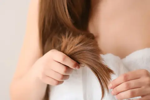Une femme examine ses cheveux, cherchant des conseils pour comment éviter les fourches et garder une chevelure saine.