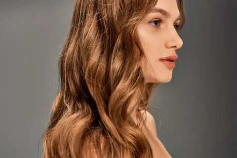 Une femme aux cheveux châtains ondulés, une transformation réussie de blonde à brune, pose de profil.