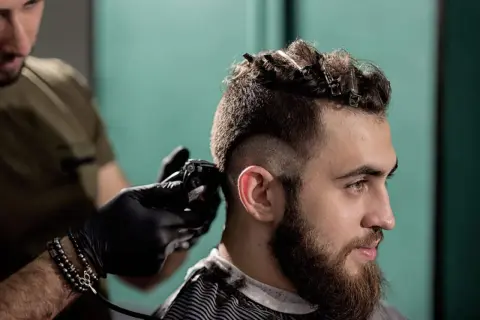 Un homme se fait couper les cheveux en coupe mohawk court par un coiffeur.