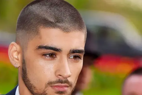 Un jeune homme au regard intense arbore une coupe buzz, ses cheveux courts et nets accentuent son style moderne.