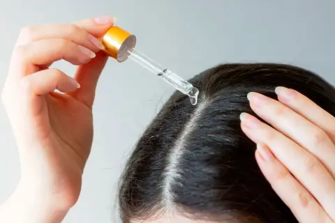 Une main applique une goutte d'huile de chanvre sur le cuir chevelu, une solution naturelle pour les cheveux blancs.