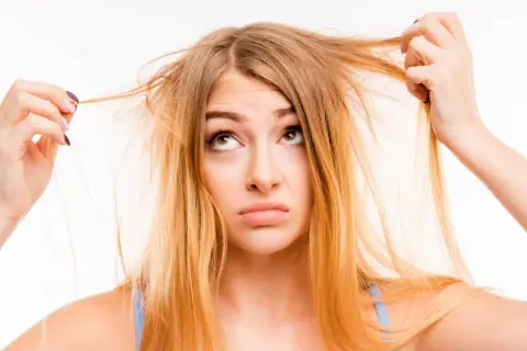 Une jeune femme aux cheveux jaune regarde ses mèches emmêlées avec une expression perplexe.