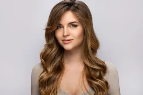 Une jeune femme au regard captivant, ses longs cheveux méchés ondulés encadrant son visage.