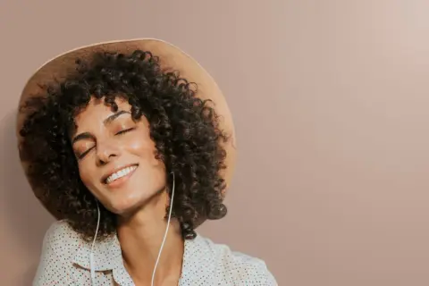 Femme avec une permanente naturelle, un chapeau et des écouteurs, profitant d'un moment de détente.