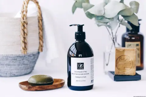 Savon liquide d'Alep pour les cheveux, avec un savon solide et une bouteille pompe. Un panier en osier est visible en arrière-plan.