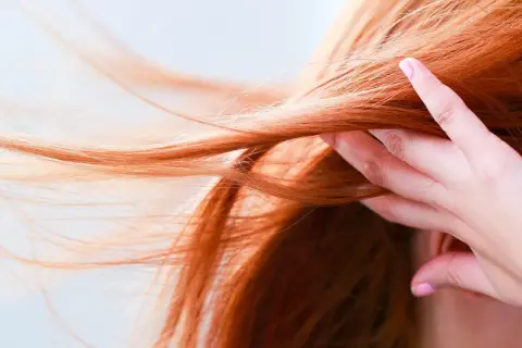 Chevelure rousse flamboyante, une main effleure les mèches. Quelle coloration pour enlever le roux ?
